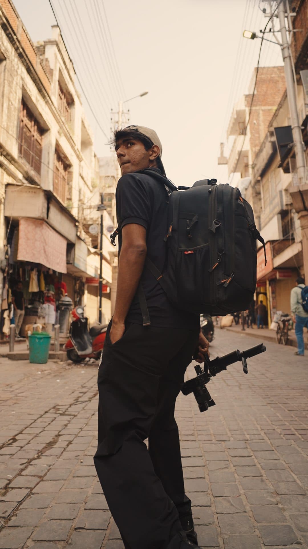 Crew member with a backpack and camera rig in a narrow old-city street